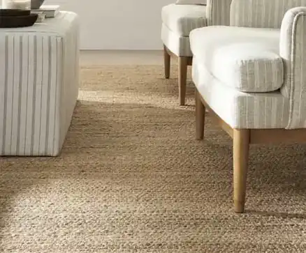 Natural textured rug beneath cream striped armchairs and a matching footstool