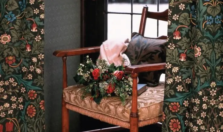 Interior scene with a wooden chair framed by Blackthorn fabric by Morris & Co featuring rich floral and foliage patterns