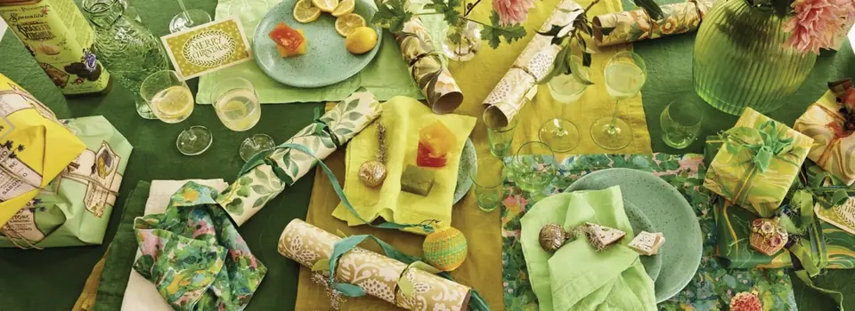 Festive table setting styled with green and yellow fabrics and wallpapers from Designers Guild, featuring wrapped gifts, crackers, glassware and citrus accents
