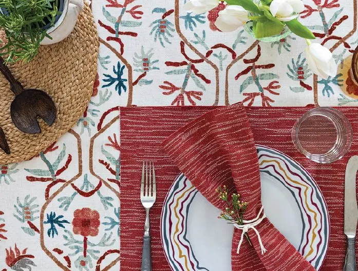 Table setting styled with red napkins and plates on floral fabric from the L'eternel Ete collection by GP & J Baker