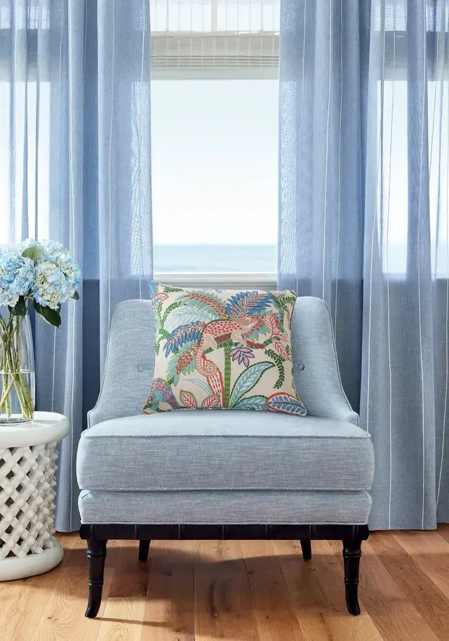 Blue coloured sheer curtains filtering daylight around a contemporary armchair