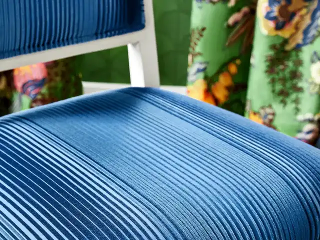 Bright blue ribbed upholstery on a chair beside a green patterned curtain