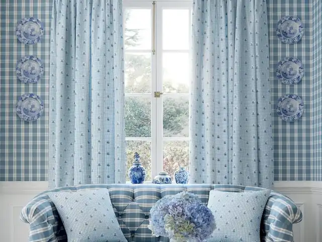 Pale blue embroidered curtains beside a window in a blue and white room