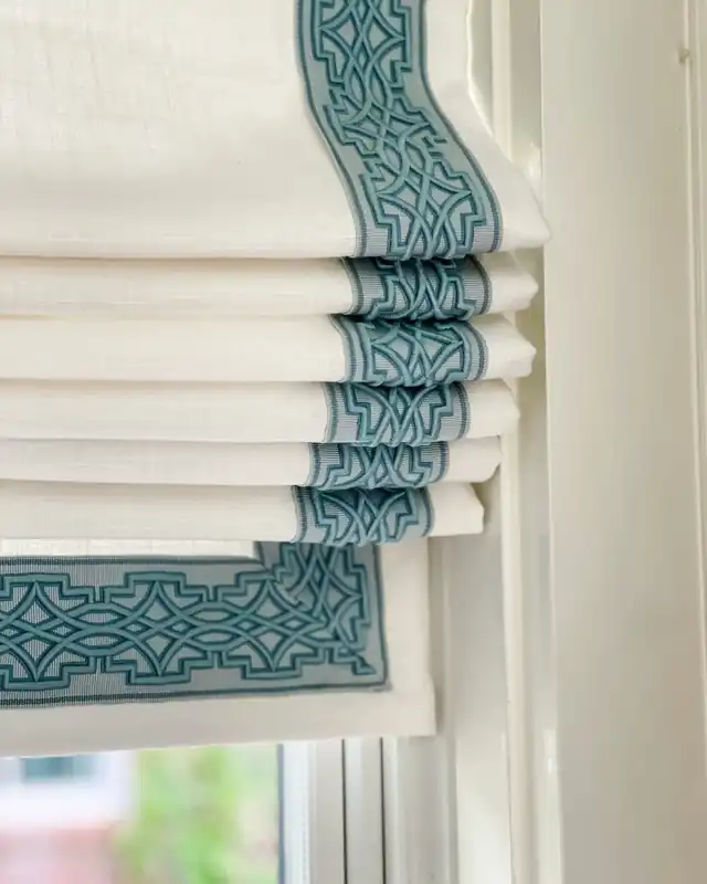 Cream Roman blind with teal geometric braid framing the edges and continuing through the folds