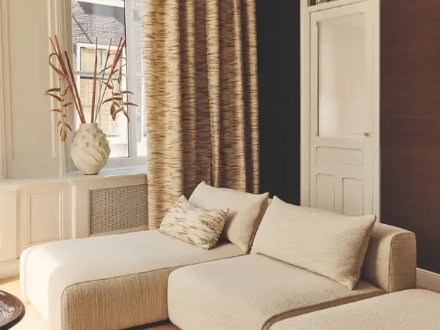 Cream corner seating and cushions beside brown patterned curtains