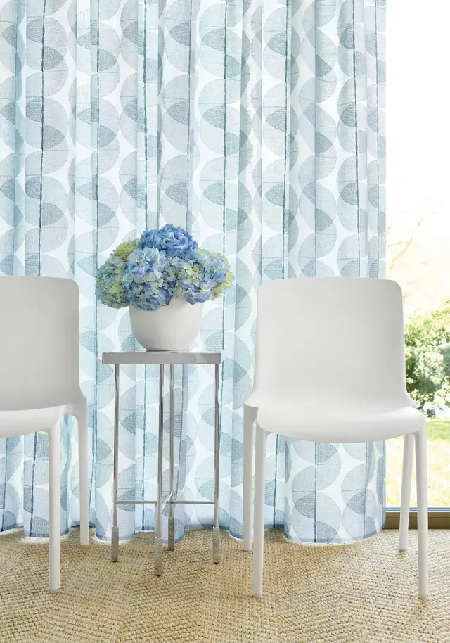 Blue embroidered voile curtain fabric displayed across a full-height window
