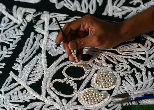 Close-up of embroidered wallcovering being hand finished with stitched and beaded detail
