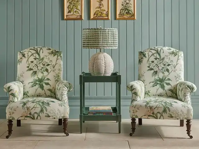 Two armchairs in green botanical fabric against painted green panelling