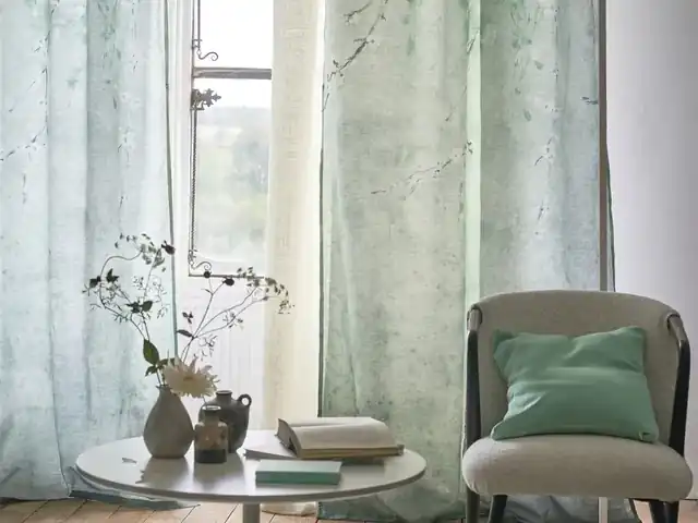 Pale green patterned curtains beside a chair with a green cushion