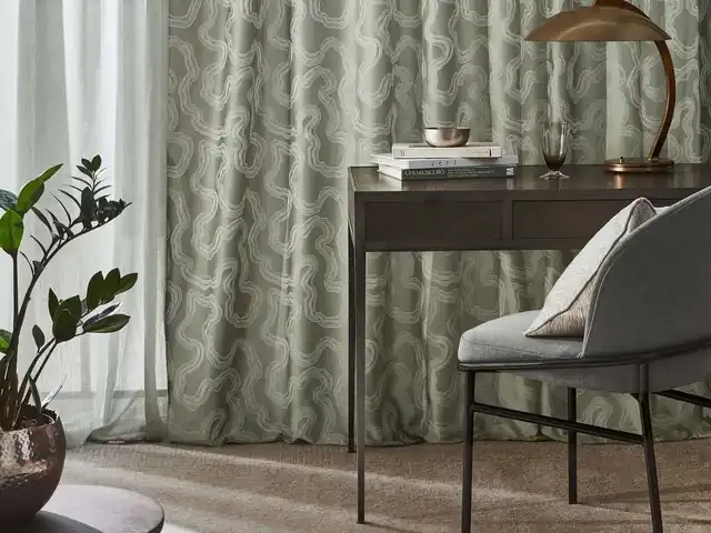 Soft grey patterned curtains beside a desk and grey upholstered chair