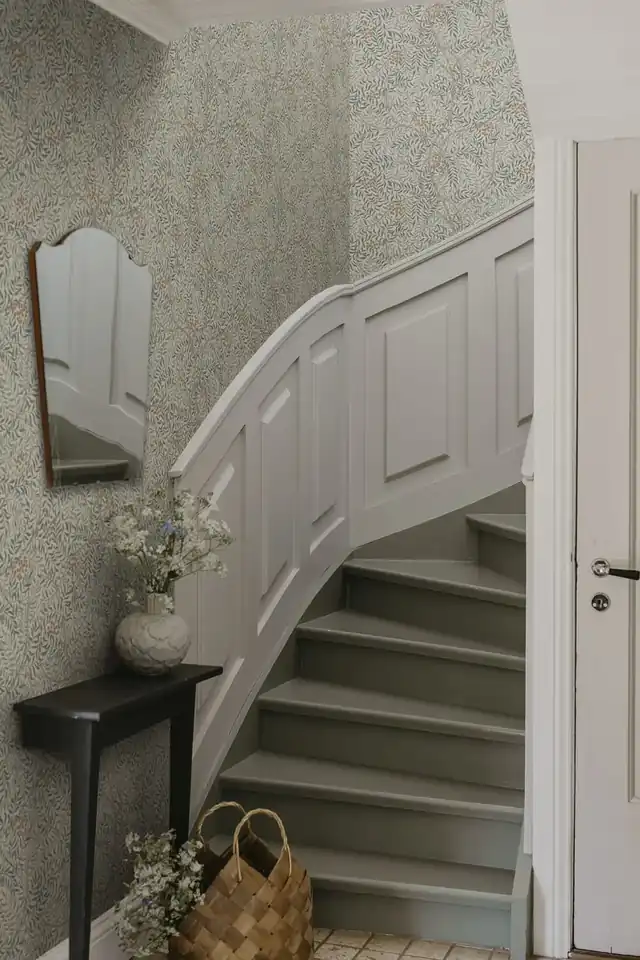 Patterned hallway wallpaper installed above painted staircase panelling