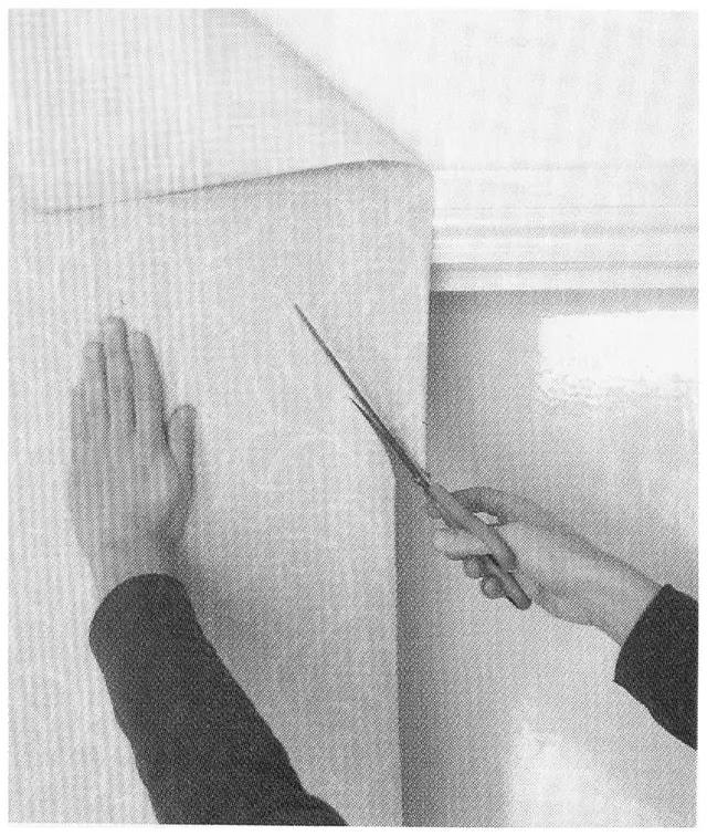 Photograph showing a relief cut being made in wallpaper at the top corner of a door frame