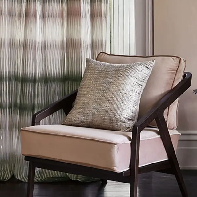 Metallic sheer curtain fabric filtering daylight beside an upholstered chair