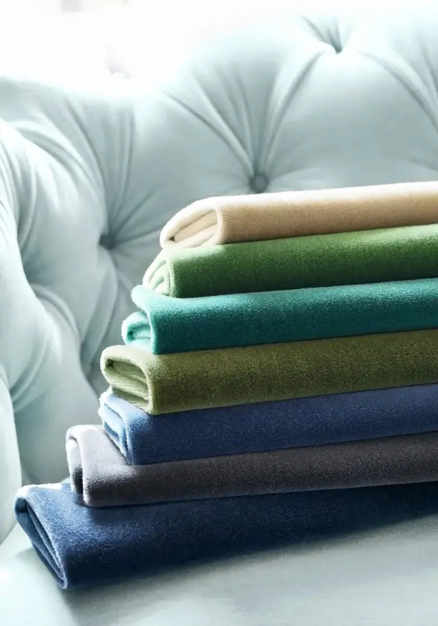 A stack of coloured mohair velvet fabrics beside a pale blue upholstered sofa