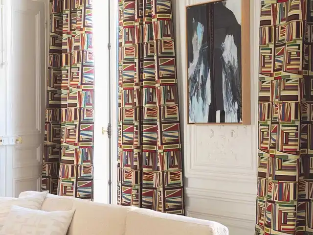 Geometric curtains combining red, green and neutral tones beside a pale sofa
