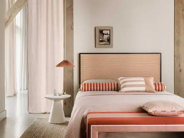 Bedroom with a pale pink upholstered headboard, striped cushions and warm-toned bedding