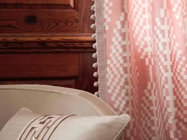 Pink and cream ikat curtain beside a pale upholstered chair and wooden panelling