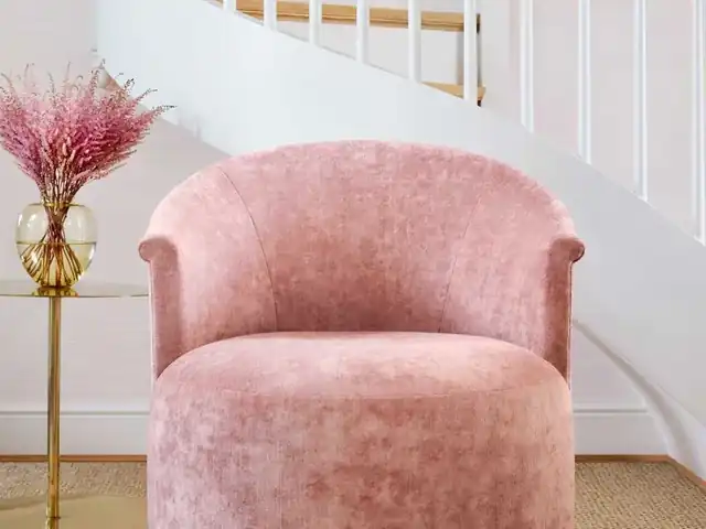 Pink velvet upholstered chair beside a white staircase