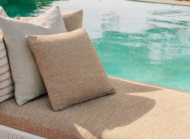 Neutral textured outdoor cushions arranged beside a swimming pool