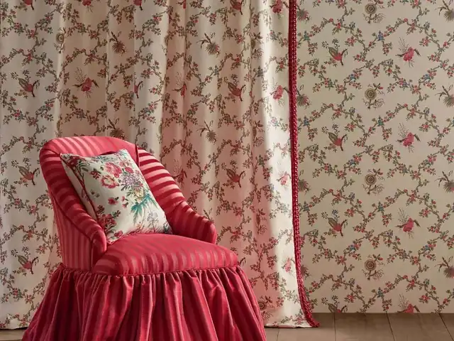 Red upholstered chair and floral cushion beside pale patterned curtains with red details