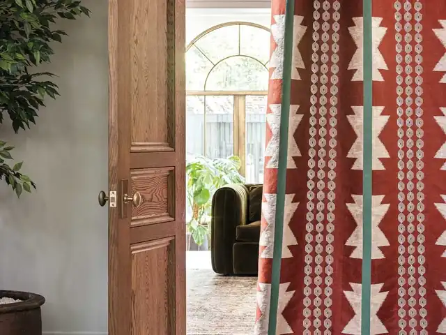 Red and cream geometric curtain with green accents beside a wooden doorway