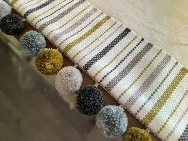 Striped Roman blind fabric with multicoloured pom-pom trim in the TM Interiors workroom