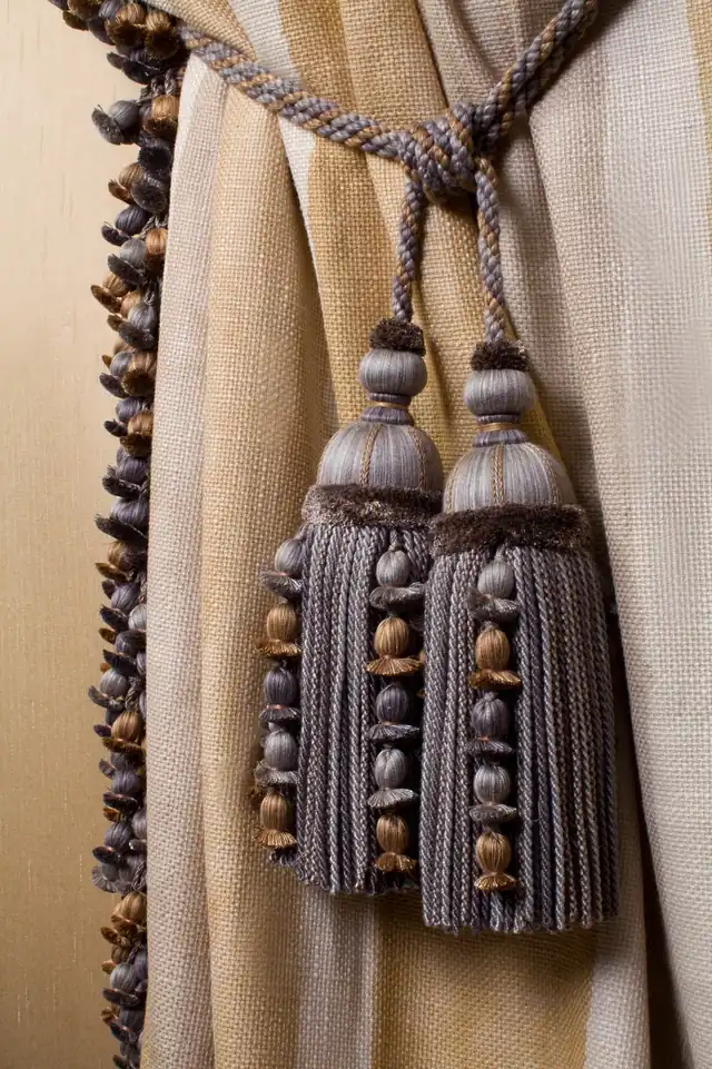 Decorative double tassel tieback beside coordinating fringe on a neutral curtain
