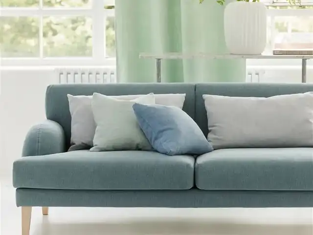 Muted blue-green woven sofa with pale cushions and light green curtains