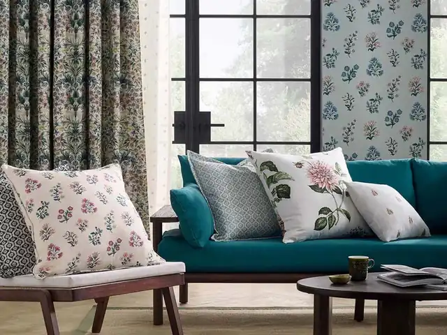 Deep turquoise sofa with pale patterned cushions beside botanical curtains
