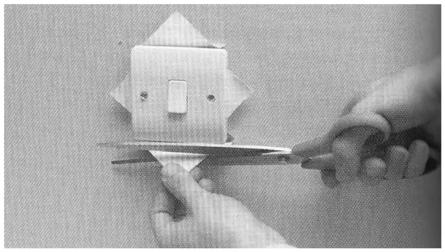 Step-by-step photograph showing diagonal relief cuts around a light switch before trimming