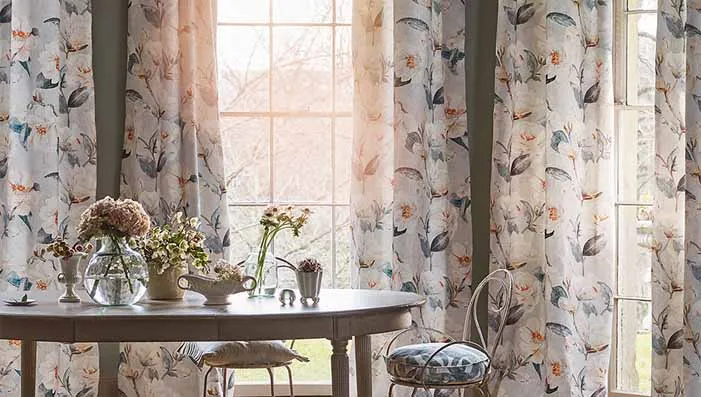 A beautifully lit dining room with floral and botanical patterned curtains, highlighting vibrant flowers and greenery, perfect for a nature-inspired decor theme.